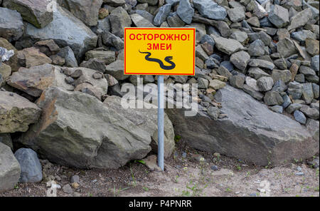 Warnschild "Vorsicht: Schlangen in einem Russischen. Warnschild an Ort und Stelle es Schlangen leben. Große Steine von Rock auf den Hintergrund. Russland, Wladiwostok. Stockfoto