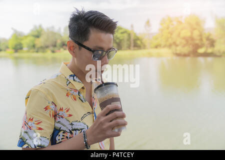 Asiatischer Mann genießen Kaffee kalt in Pastic Glas mit nach Hause nehmen, trinken, auf den Fluss und die Berge Natur Hintergrund; Urlaub Ferien portrait Konzept in Vintage Stockfoto