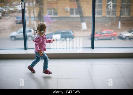 Ein kleines Mädchen läuft rund um die neue große Wohnung in der Nähe von einem Panoramafenster Stockfoto