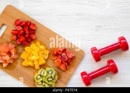 Gehackte bunte rohe Früchte und Kurzhanteln auf weißem Holz- Hintergrund, Ansicht von oben. Kopieren Sie Platz. Stockfoto