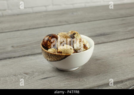 Gefleckte Wachteleier in kleinen Porzellan Schüssel auf grau Holzschreibtisch. Stockfoto