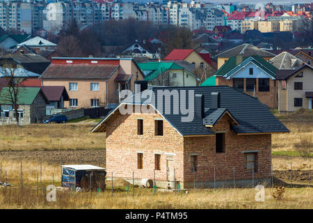 Marke neue geräumige brick Zweistöckiges Wohnhaus mit Fliesen Dach und Fenster Öffnungen in Suburban Nachbarschaft auf dem Hintergrund der fernen Stadt. buil Stockfoto