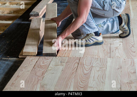 Nahaufnahme von professionelle Tischler Installation von natürlichen Holz- neue Planken auf Estrich in leeren unfertiges Zimmer unter Rekonstruktion. Verbesserung, re Stockfoto