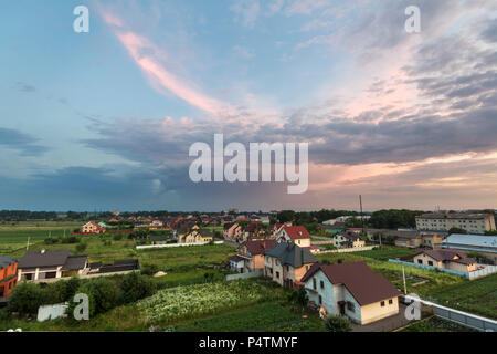 Breite Sommer Panorama der neuen ruhigen Vorort. Grundstücke und neue moderne Häuser unter grünen Bäumen bei bewölktem Himmel bei Sonnenuntergang. Constructi Stockfoto