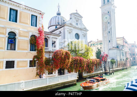 Klassische Motorboot mit zwei ständigen Touristen und Geschäftsreisende, die Chiesa San Giorgio (Griechische Kirche) am Rio del Greci im hellen Sonnenschein und Farben, Venedig, Italien. Stockfoto