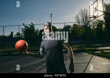 Portrait von tätowierten jungen Mann mit Basketball auf Gericht Stockfoto