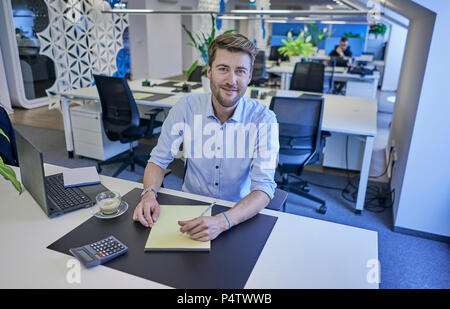 Portrait von lächelnden Geschäftsmann am Schreibtisch sitzen in open-plan Office Stockfoto