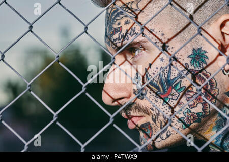 Tätowierten Gesicht der jungen Mann hinter Zaun Stockfoto