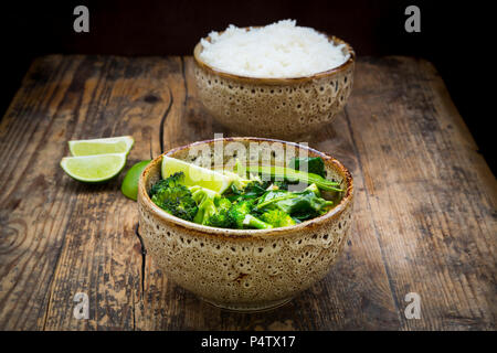 Green Thai curry mit Broccoli, Pak Choi, Zuckerschoten, Baby Spinat, Kalk und Schüssel Reis im Hintergrund Stockfoto