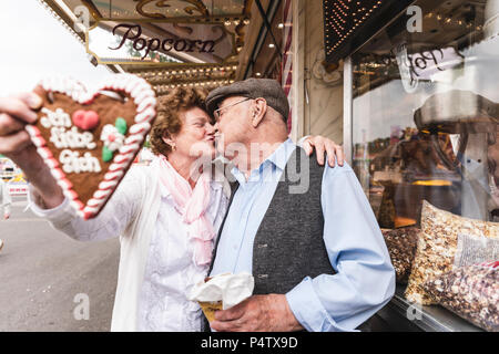 Senior Paar mit Lebkuchenherz küssen auf Messe Stockfoto