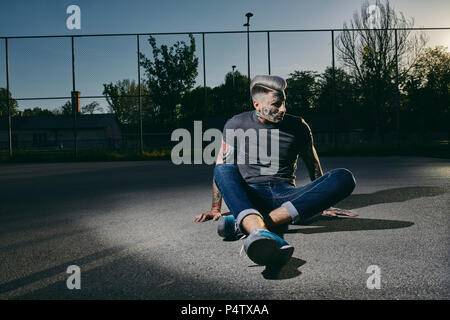 Tätowierte junge Mann sitzt auf Basketball bei Sonnenuntergang Stockfoto