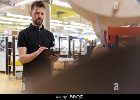 Mann mit Zwischenablage in der Fabrik von Notizen Stockfoto