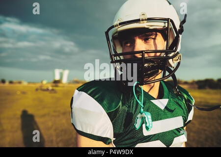 Junge Fußballspieler das Tragen eines Helmes allein stehend auf einer Wiese bei einem späten Nachmittag Training Stockfoto