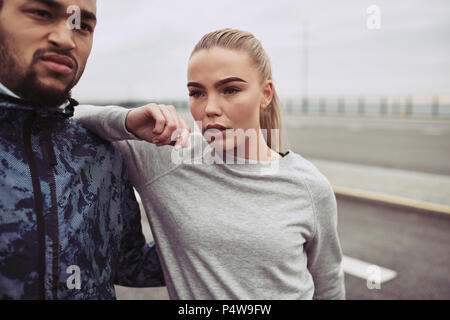 Diverse junge Paar stehen gemeinsam auf einer Straße eine Pause aus einem Lauf an einem bewölkten Tag Stockfoto