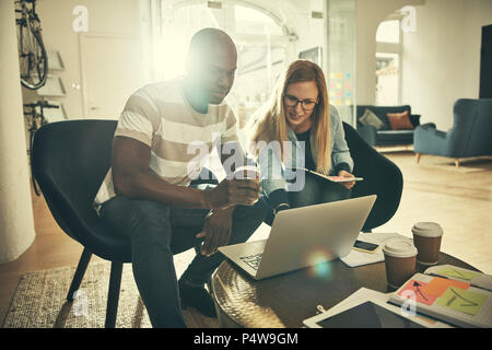 Zwei junge Designer arbeiten gemeinsam an einem Projekt mit einem Laptop während der Sitzung in einem stilvollen, modernen Büro Stockfoto