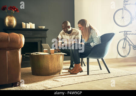 Zwei vielfältige Design Profis sitzen in einem stilvollen, modernen Büro reden und online arbeiten mit einem Laptop Stockfoto