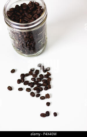 Kaffee Bohnen im Glas und Kaffeebohnen auf einer weissen Fläche angezeigt Stockfoto