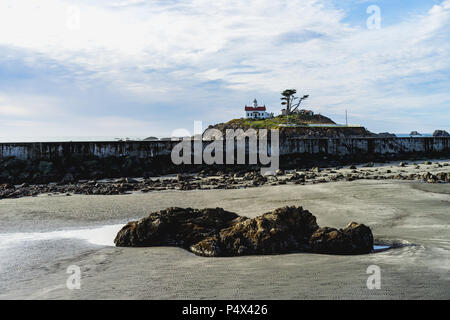 Strand bei Ebbe mit einem Felsen im Vordergrund und ein Leuchtturm im Hintergrund Stockfoto