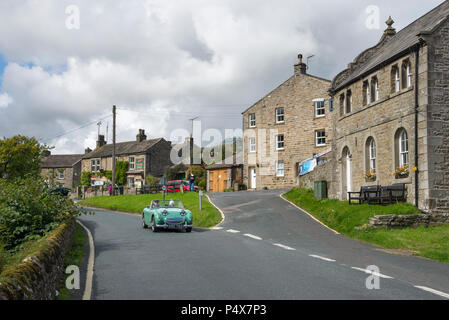 Paar fahren Oldtimer durch das Dorf Muker in Swaledale, Yorkshire Dales, England. Stockfoto