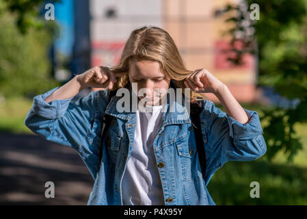 Das kleine Mädchen Teenager. Sommer in der Natur. In denim Kleidung hinter Rucksack gekleidet. Die Geste schließt die Ohren mit den Händen. Augen sind geschlossen. Konzept der Stille und der Unwissenheit. Emotionen laut Skandal. Stockfoto