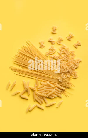 Verschiedene verschiedene Roh rohe Nudeln auf gelben Hintergrund. Italienische Pasta: Penne, Farfalle, Spaghetti. Stockfoto
