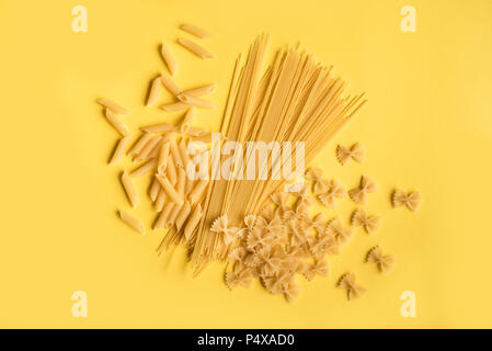 Verschiedene verschiedene Roh rohe Nudeln auf gelben Hintergrund. Italienische Pasta: Penne, Farfalle, Spaghetti. Stockfoto