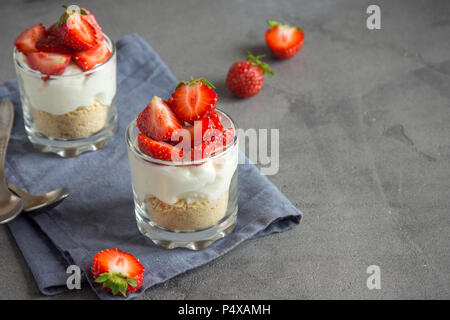 Strawberry trifle Mini Dessert in Gläsern mit frischen Erdbeeren und Sahne Käse auf grauem Beton Hintergrund. Gesunde hausgemachte potrion Dessert. Stockfoto