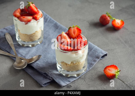 Strawberry trifle Mini Dessert in Gläsern mit frischen Erdbeeren und Sahne Käse auf grauem Beton Hintergrund. Gesunde hausgemachte potrion Dessert. Stockfoto