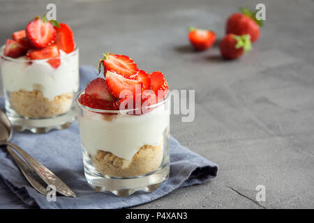 Strawberry trifle Mini Dessert in Gläsern mit frischen Erdbeeren und Sahne Käse auf grauem Beton Hintergrund. Gesunde hausgemachte potrion Dessert. Stockfoto