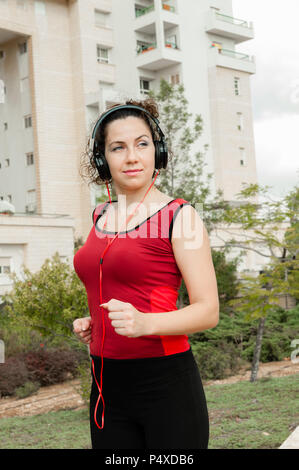 Das Mädchen ist im Sport in der Stadt Park, Joggen und Hören auf das Mädchen ist im Sport engagiert und das Hören von Musik über Kopfhörer Stockfoto