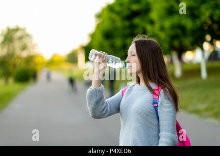 Mädchen Schülerin im Sommer im Freien. Er hält eine Flasche Wasser in der Hand. Freier Platz für Text. Das Konzept reines Wasser. Emotionen geniessen, die Ruhe nach der Schule, Durst. Stockfoto