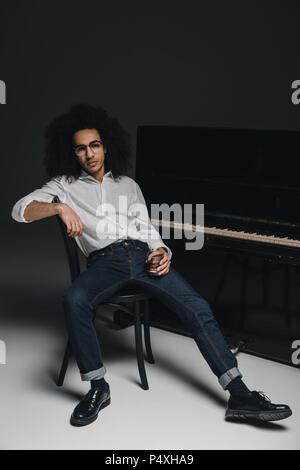 Schöne stilvolle Musiker mit Glas Whisky vor Piano Stockfoto