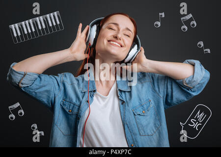 Junge Frau lächelnd und schließen Ihre Augen, während Sie Musik hören Stockfoto