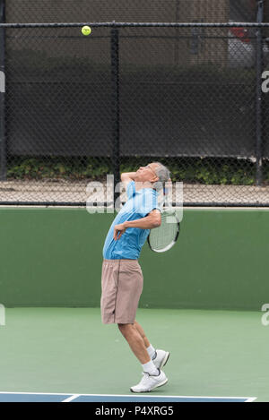 Aktive chinesische Senioren tennis player fokussiert auf die Kugel in der Luft mit Schläger zurück für eine Stromversorgung dienen. Stockfoto