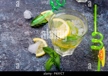 Frische kalte Mojito Cocktail mit Soda, Eis, Minze und Zitrone im Glas und Zutaten auf einem dunklen Hintergrund, Kopieren spase, selektiver Fokus Stockfoto