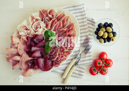 Kalt geräucherte Fleisch Platte mit Schweinefleisch, Schinken, Salami, Bresaola mit schwarzen und grünen Oliven und Tomaten cherry auf weißem Holz- Hintergrund für t serviert. Stockfoto