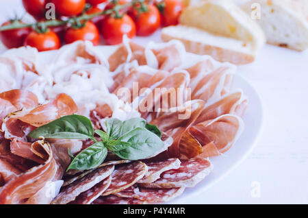 Kalt geräucherte Fleisch Platte mit Schweinefleisch, Schinken, Salami, Bresaola und Basilikum auf weißem Holz- Hintergrund. Wein Vorspeise gesetzt. Italienisches Essen. Stockfoto