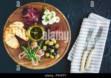 Auswahl an spanischen Tapas oder italienische Antipasti: Schinken, Bresaola, Mozzarella, getrocknete Tomaten, Oliven und Toast auf Holzbrett. Noch l Stockfoto