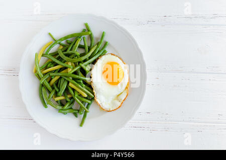 Gekochte grüne Bohnen mit Spiegelei in Weiß Platte auf Holz- Hintergrund mit Platz für Text. Gesunde vegetarische Essen Konzept. Ansicht von oben. Kopieren Sie Platz. Stockfoto