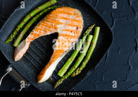 Gegrilltes Lachssteak und Spargel auf Grill Pfanne auf schwarzen Stein Hintergrund. Gesunde Ernährung Konzept. Ansicht von oben. Kopieren Sie Platz. Stockfoto