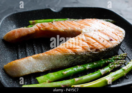 Gegrilltes Lachssteak und Spargel auf Grill Pfanne auf schwarzen Stein Hintergrund. Gesunde Ernährung Konzept. Close Up. Stockfoto