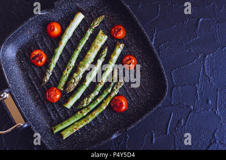 Gegrillter grüner Spargel und Tomaten cherry am Grill zubereitet Pan Am schwarzen Stein Hintergrund mit Platz für Text. Gesunde Ernährung Konzept. Ansicht von oben. Kopieren Stockfoto