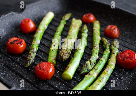 Gegrillter grüner Spargel und Tomaten cherry am Grill zubereitet Pan Am schwarzen Stein Hintergrund. Gesunde Ernährung Konzept. Stockfoto