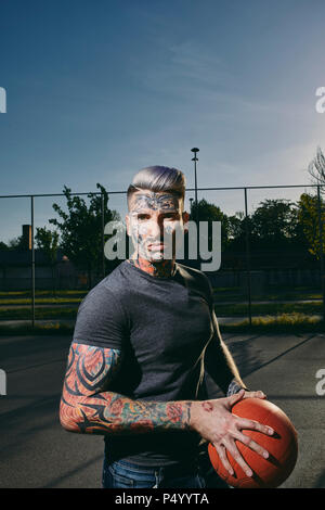 Portrait von tätowierten jungen Mann mit Basketball auf Gericht Stockfoto