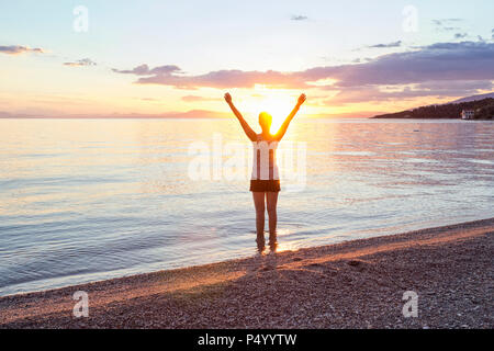 Griechenland, Pilion, Pagasäischen Golf, Frau am Strand mit erhobenen Armen bei Sonnenuntergang, Kalamos im Hintergrund Stockfoto