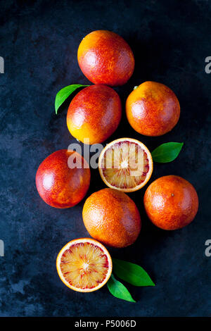 Ganze und aufgeschnittene Blutorangen auf dunklem Boden Stockfoto