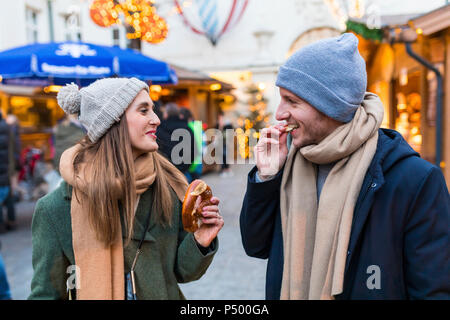 Junges Paar Brezel zusammen essen am Weihnachtsmarkt Stockfoto