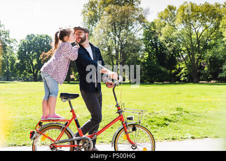 Tochter küssen Vater mit dem Fahrrad in einem Park Stockfoto