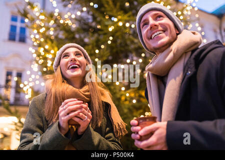 Lachende junge Paar trinken Glühwein am Weihnachtsmarkt Stockfoto