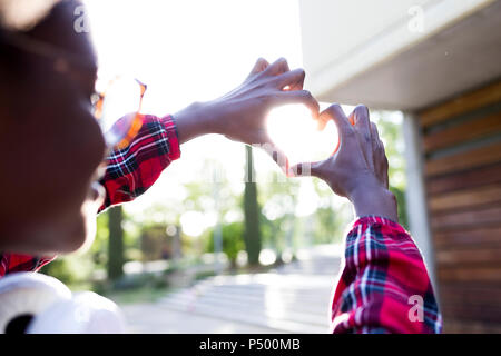 Junge Frau Gestaltung Händen ein Herz gegen Sonnenlicht Stockfoto